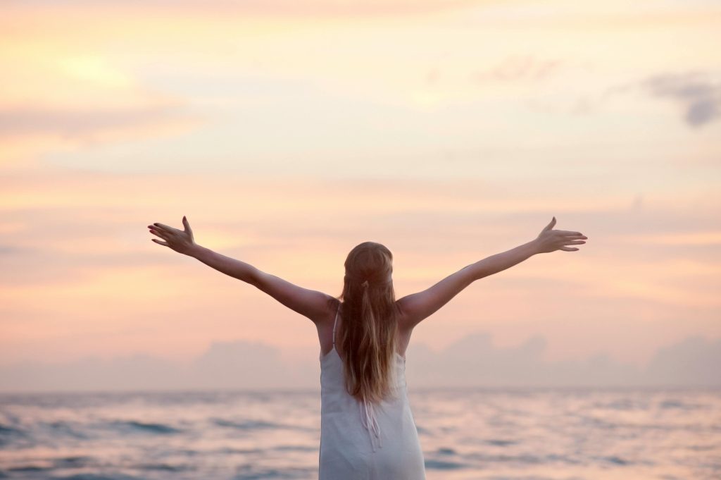Rear view of woman with arms raised at beach during sunset